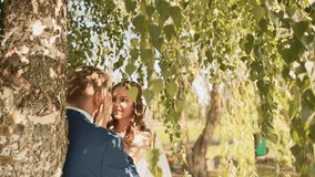 Beautiful and happy bride and groom under the branches of the birch trees rejoice together. Touching hands.