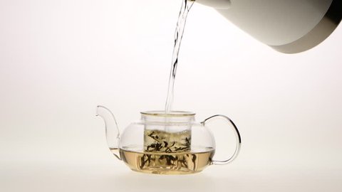 Leaves of green tea are brewed in teapot, white background