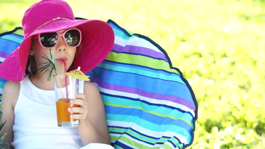 Closeup portrait of a girl drinking juice and sitting in a chair outdoors
