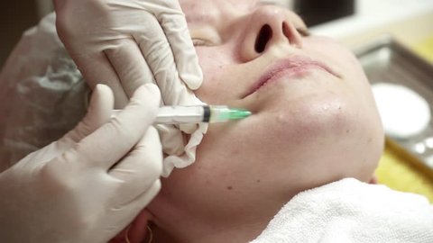 Beautician making anti aging injections to cheek for the woman closeup