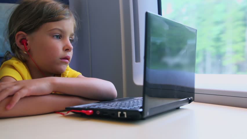 Little girl watch on netbook when sits at train near window