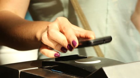 closeup  female hand with manicure bring the phone to  ntfs system reader in metro turnstile for payment of fare