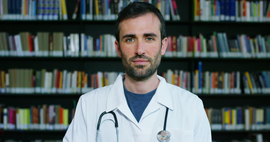 A young and beautiful doctor in a library smiling happy and holding books after doing a search and after studying. Concept: educational, portrait, library, and medical care and welfare