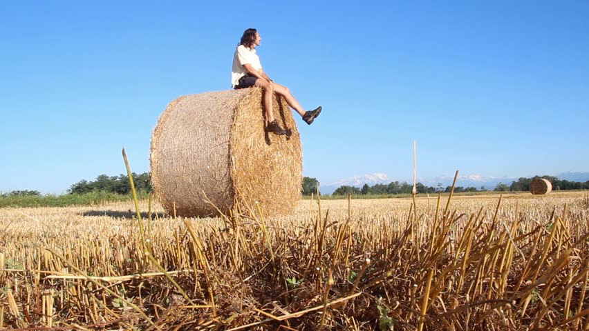 man popping around Baled hay in a Rolling Farm Field