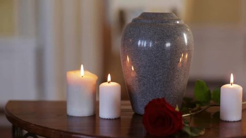 funeral, cremation, mourning and burial concept - funerary urn and candles on table burning indoors