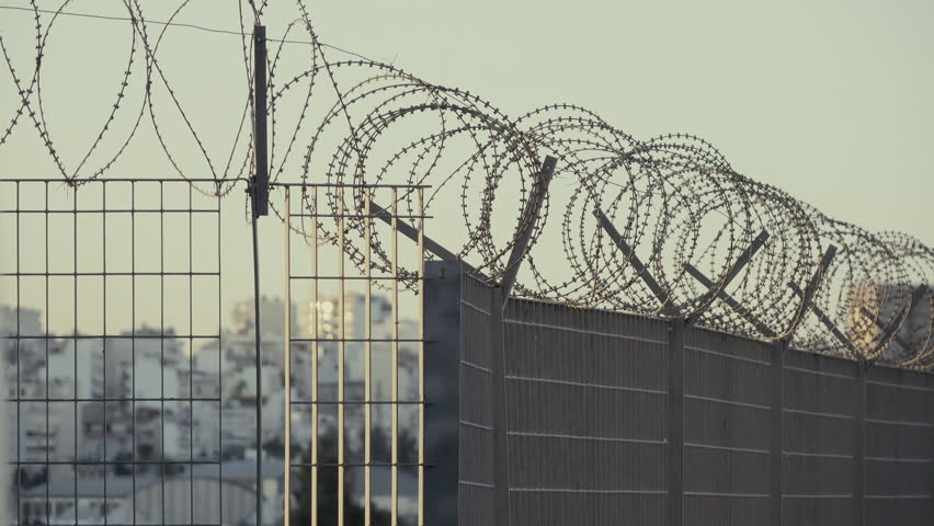 A city skyline in the morning obscured by a steel fence covered with razor wire. Royalty-Free Stock Footage #25542131