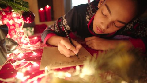 Teen girl is lying near decorated christmas tree and writing christmas letter to Santa Claus