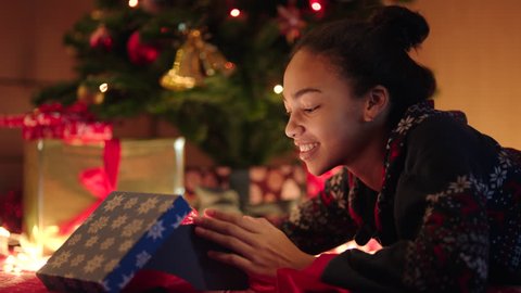Young black woman is openning a gift box with red ribbon on New Years night, videoclip de stoc