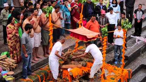 KATHMANDU, NEPAL - MAY 24, 2016: Men put wooden logs on body preparig for cremation. People around pray. Pashupatinath temple complex that is on UNESCO World Heritage Sites's list Since 1979
