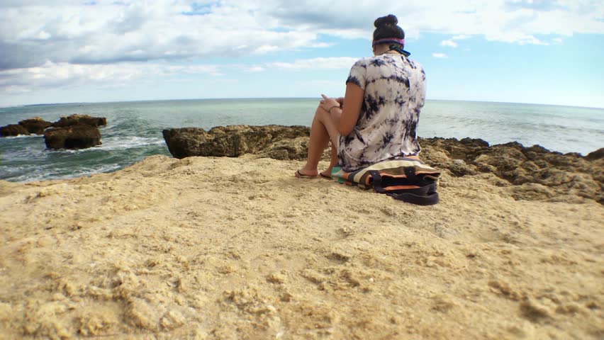 Young Woman On Beautiful Landscape Watching Ocean View, Wide Angle. Girl looking at the ocean on a high cliff edge sitting alone.