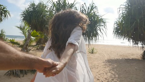 Girl holding male hand and running on tropical exotic beach to the ocean. Follow me shot of young woman pull her boyfriend on the sea shore. Summer vacation or holiday. Point of view. POV Slow motion