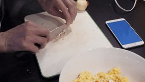 Male hands cutting garlic at home kitchen. Young man preparing vegetable food and watching video at smartphone with blue chroma key