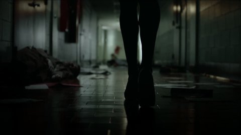 A silhouette shot of a woman walking down a dark and messy school hallway, pans up from her feet to her waist