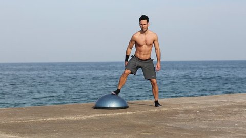 Athletic man making exercise on balance platform by the sea