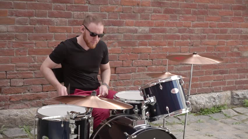 Man Playing Drums on the Street on the Background of a Brick Wall
