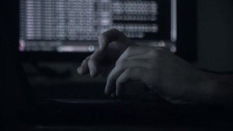 The hacker hacks the server with bank accounts in a dark room on a black background in the dark. The concept of cyber attacks and the Cold War on the Internet