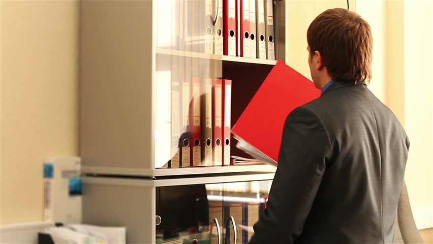 Shelf with folders for documents. Business man near the shelves with folders.