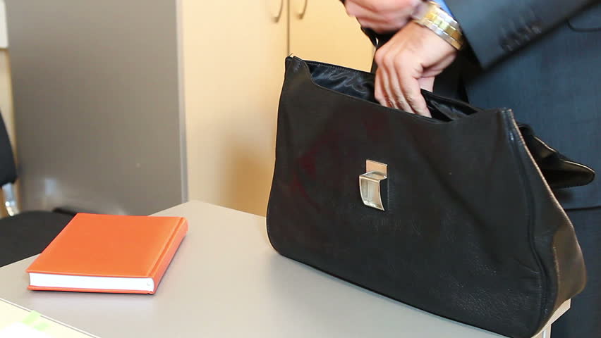 Close-up of leather briefcase in male hand. Man putting notebook into his bag.