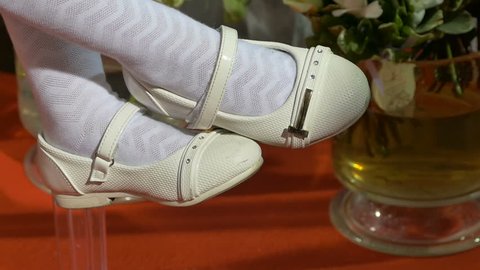 Legs of a little girl in white socks in white shoes