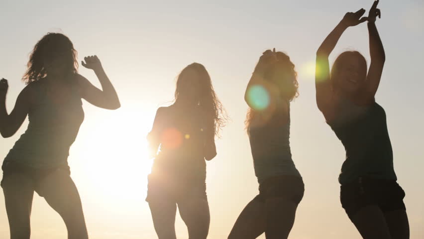 Four slim women dancing over sun on the beach