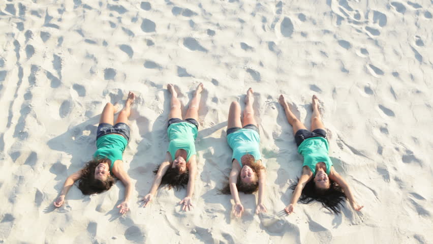 Four attractive women falling on the sand at summer