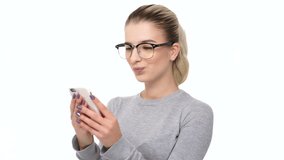 Happy satisfied young girl in eyeglasses texting message on mobile phone isolated over white