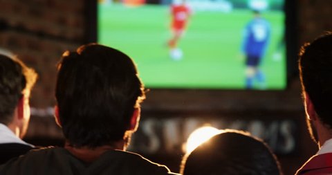 Excited friends watching soccer match while having beer in bar