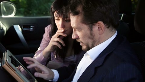 Man and woman working in car with tablet and pc 