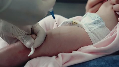 Close up shot: Doctor makes injection (leg muscle) to baby sitting in mothers arms