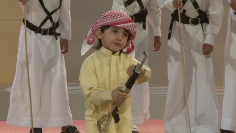 DUBAI, UAE - CIRCA 2008: View of Emirati boys dancing in traditional formation and a very young boy twirling a toy rifle, in front of judges, in an entertainment area at Dubai Festival City Mall.