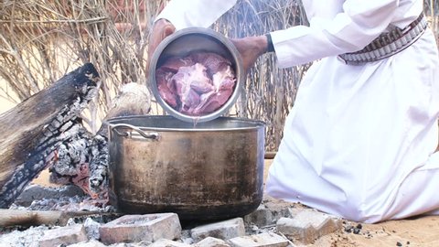 DUBAI, UAE - CIRCA 2013: MCU view of an Emirati bedouin putting fresh meat into a pot to make stew on an open campfire in the desert.