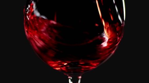 Filling wine glass with red wine super slow motion macro shot, black background