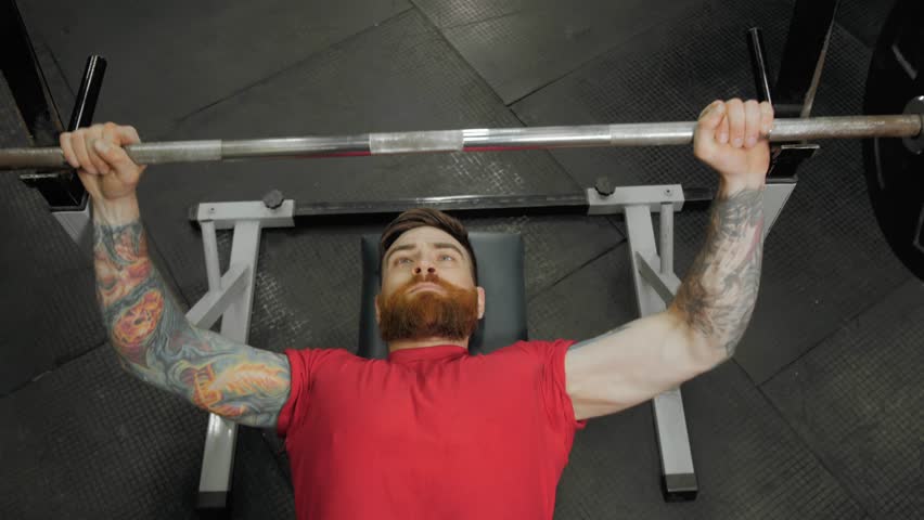 Young man lifting the barbell in the gym portrait. Steadycam follow shot of male athlete with brutal beard