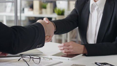 Tilt up of businessman and woman shaking hands while sitting at office table and then man taking contract and woman using digital tablet