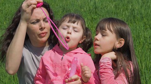 Mom and daughters in the park with soap bubbles. Happy family in the park. Children with their mother in the nature with soap bubbles. 