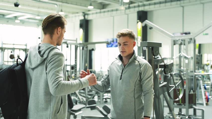 Two young fit men in gym greeting each other.