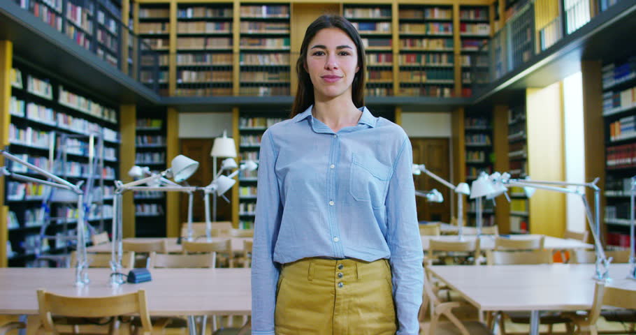 Portrait of a beautiful young woman smiling happy in a library holding books after doing a search and after studying. Concept: educational, portrait, library, and studious.