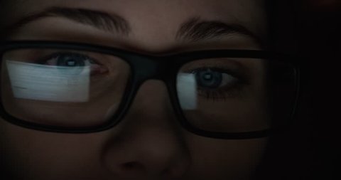 woman with glasses eyes looking at the monitor, surfing the Internet, extreme close-up, dark room