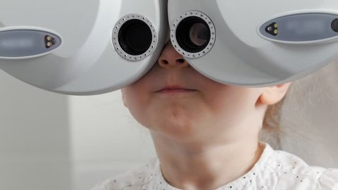Adorable little blonde girl checks eyesight at ophthalmology clinic