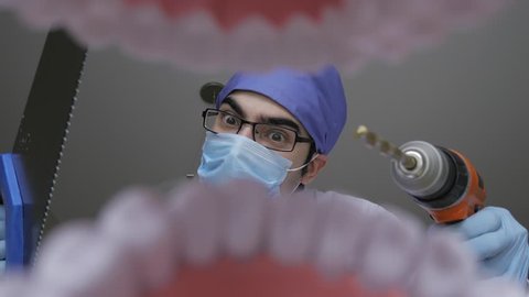 Dentist holding a wood saw and a construction drill while looking scary and dangerous. Personal or patient mouth point of view POV.