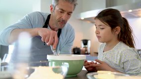 Daddy with daughter baking cake together in home kitchen
