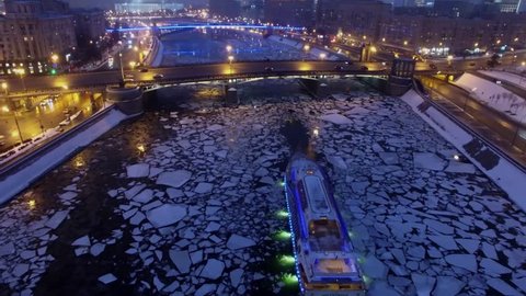 MOSCOW - JAN 22, 2017: Touristic ship Waterfly sails by Moskva river near bridge with transport traffic not far from White House at winter evening. Aerial view