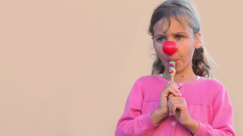 Little girl with clown nose eat colourful candy and smile