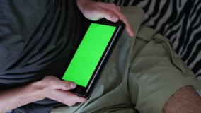 Man is Laying on Couch at Home and Watch on Tablet with Green Screen in Landscape Mode,man holds a blank tablet PC with a green screen