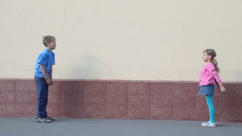 Two kids boy and little girl throws ball to each other near wall