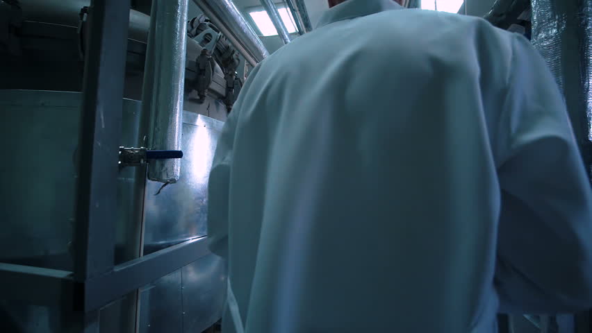 Rear view video of unrecognizable male scientist in white uniform walking through lad with metal tubes and engineering equipment aside Royalty-Free Stock Footage #25674800