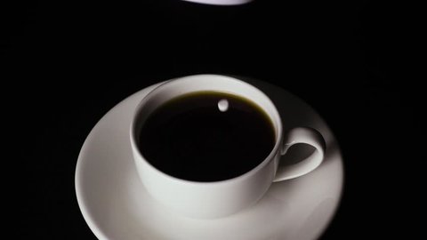 From the box sugar substitute, sweetener in pills falls into a white cup on a saucer with coffee on a black background. Slow motion