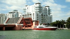 Red yacht crossing under bridge in Miami Beach, Florida, bridge lowers behind boat
