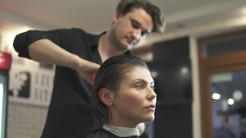 Young woman getting her hair dressed in hair salon. Stylist-hairdresser at work. Man hairdresser brushing hair in beauty saloon. Shot in slowmotion