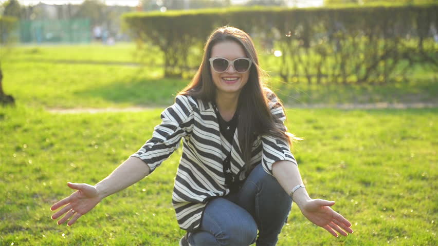 Young Mother with Long Hair and Sunglasses is Hugging her Daughter with Two Ponytails in the Park. Happy Family Enjoying Sunny Day Outdoors in Spring.